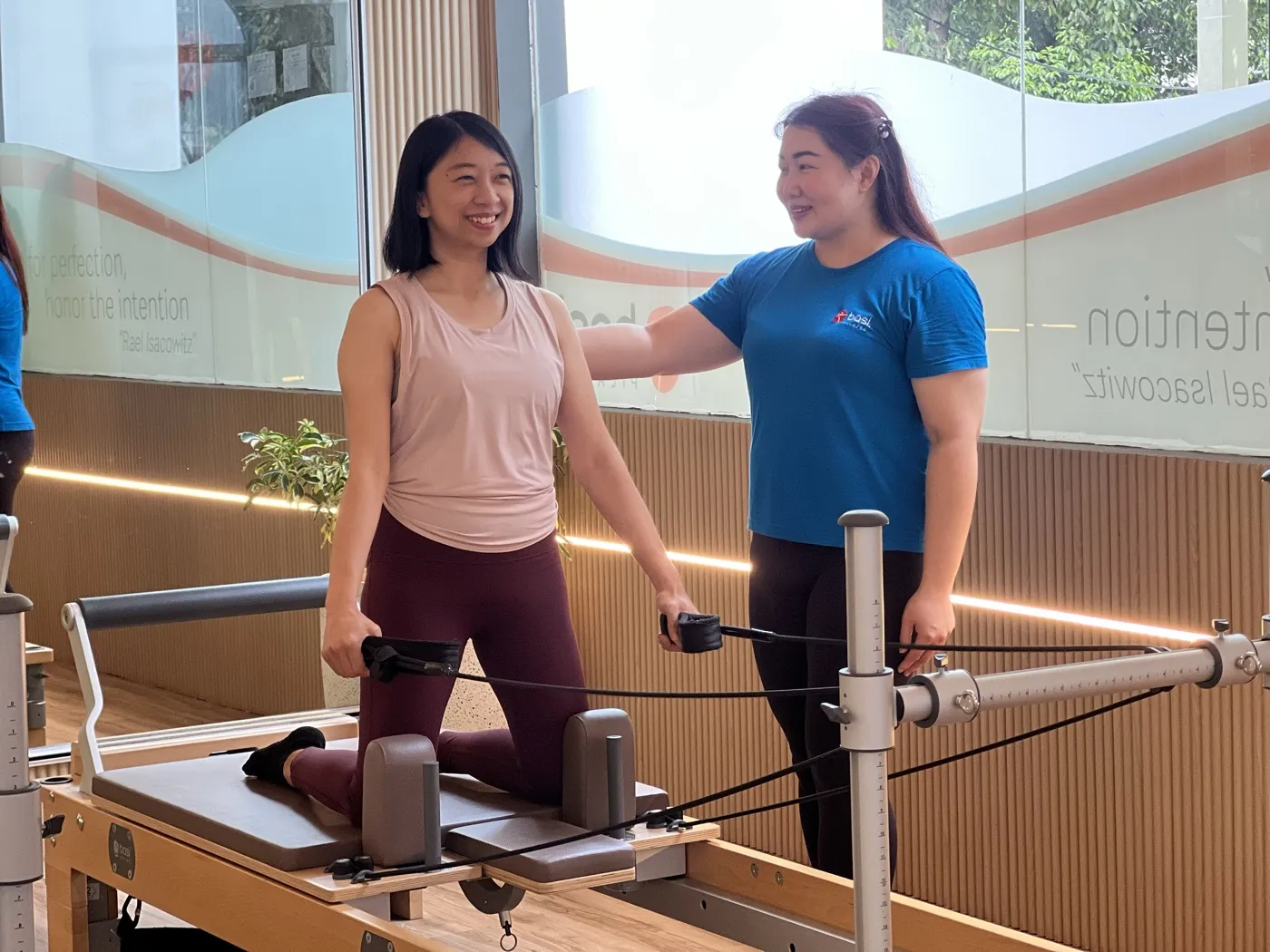 Instruktur BASI Pilates mendampingi peserta pemula di atas reformer, suasana studio hangat dan ramah
